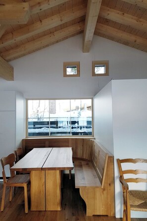 Ein Zimmer mit Holzboden, einem großen Fenster mit Blick auf eine verschneite Landschaft, einem Holztisch mit Bänken und einem Holzstuhl.