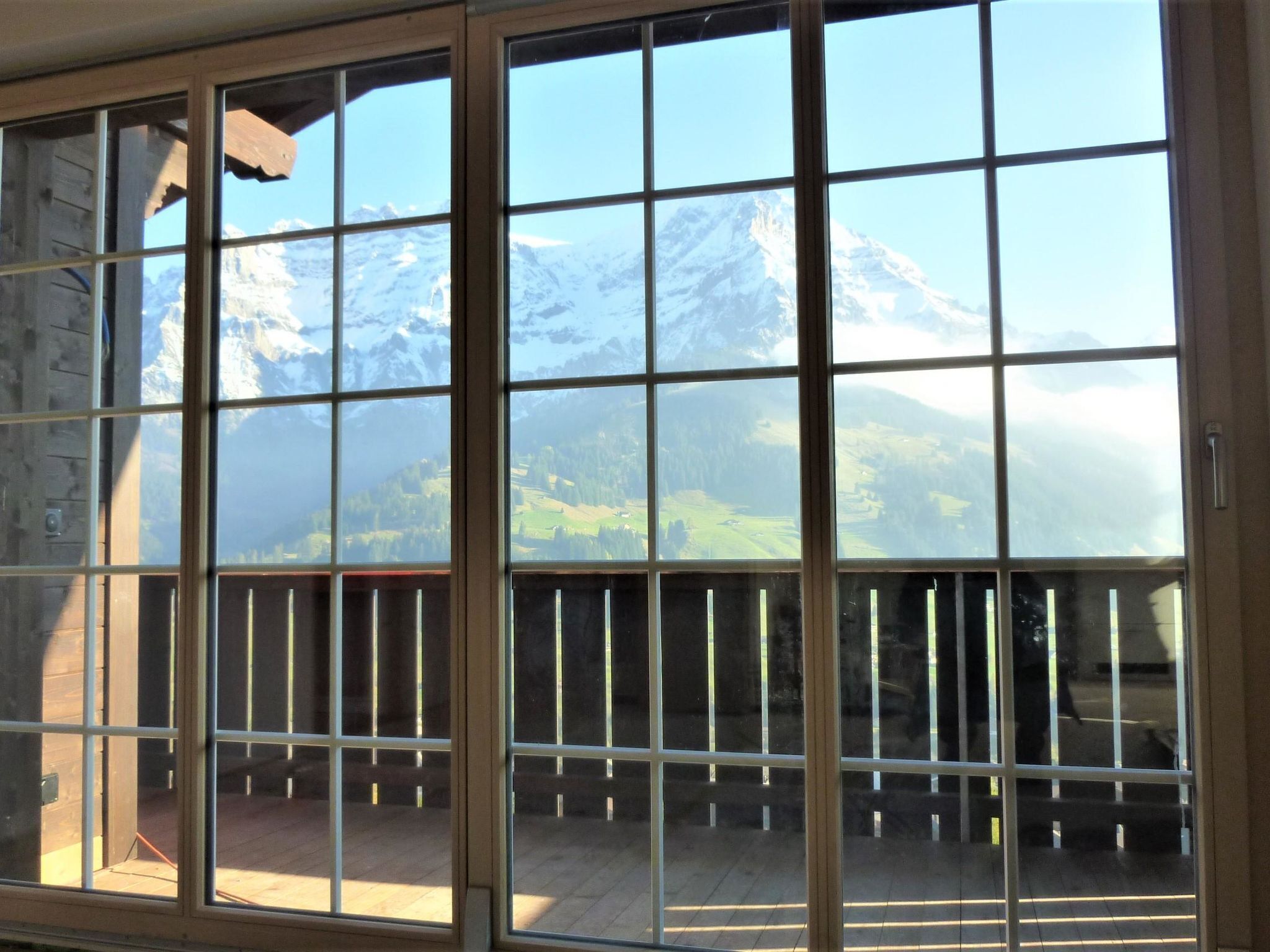 A room with a large window offering a view of snow-capped mountains and a forested valley.