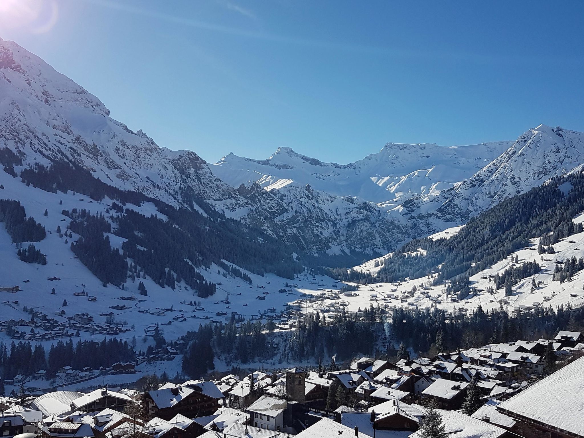 Un village de montagne enneigé, avec des bâtiments traditionnels et un ciel dégagé.