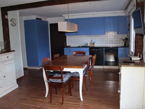 A kitchen with blue cabinets, a wooden dining table with chairs, and a hanging light fixture. - Lavendel AP C22 Appartement/Fewo, Dusche, WC, 3 Schlafräume 4-Zimmerwohnung by Interhome (Adelboden)