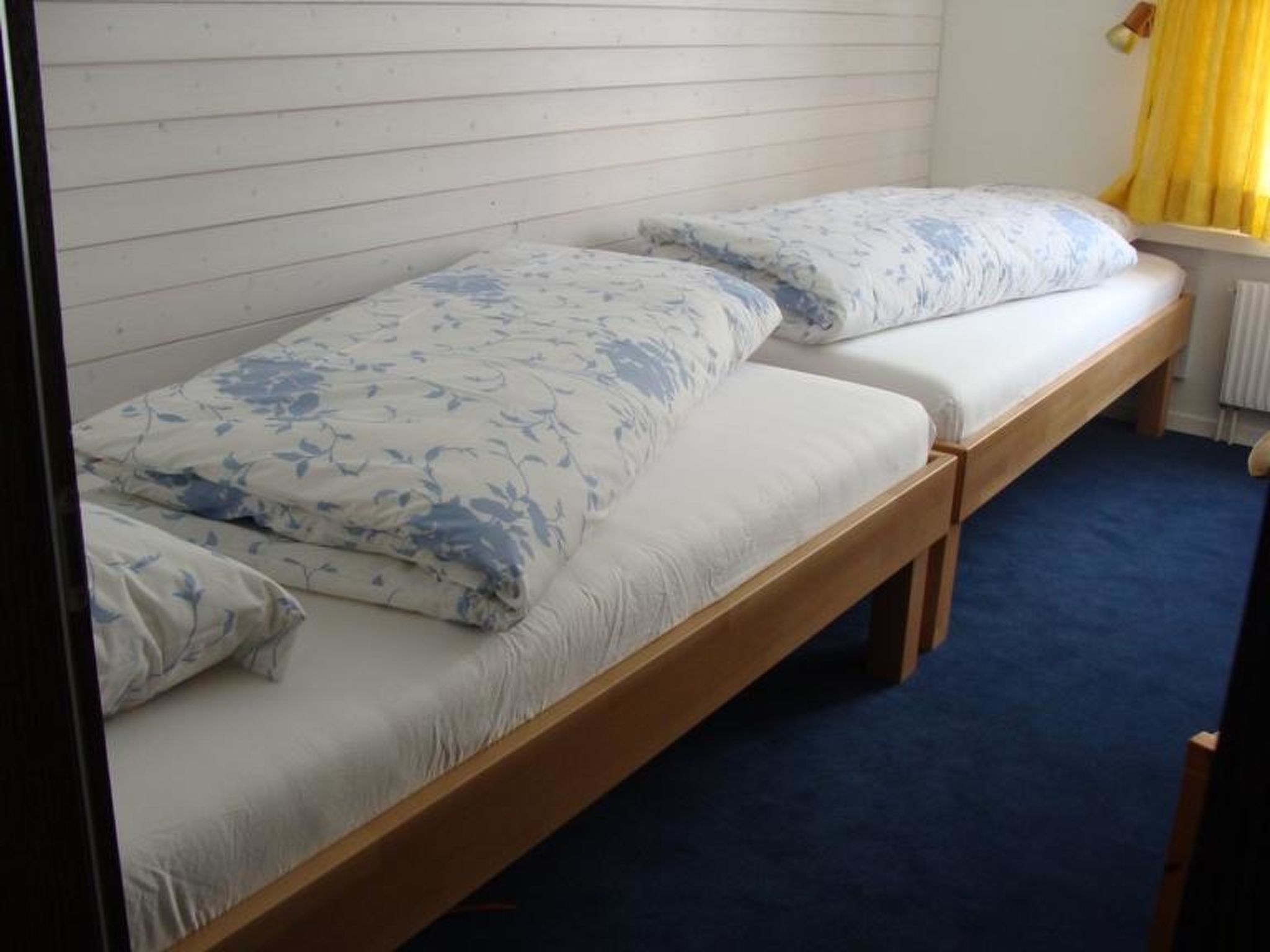 Ein Einzelbett mit einer blumigen Bettdecke und Kissen, einem Holzrahmen und einem blauen Teppich.