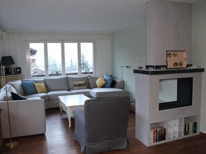 A living room with a sofa, armchair, coffee table, fireplace, and a bookshelf. - Lavendel AP C22 Appartement/Fewo, Dusche, WC, 3 Schlafräume 4-Zimmerwohnung by Interhome (Adelboden)