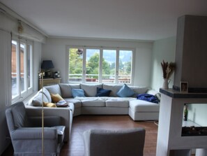 Ein Wohnzimmer mit Ecksofa, einem Sessel, einer Lampe und einem Kamin.