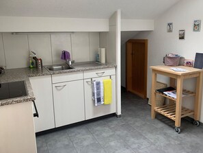 Een kleine keuken met een ingebouwde kookplaat, een spoelbak en een houten deur naar een andere kamer.