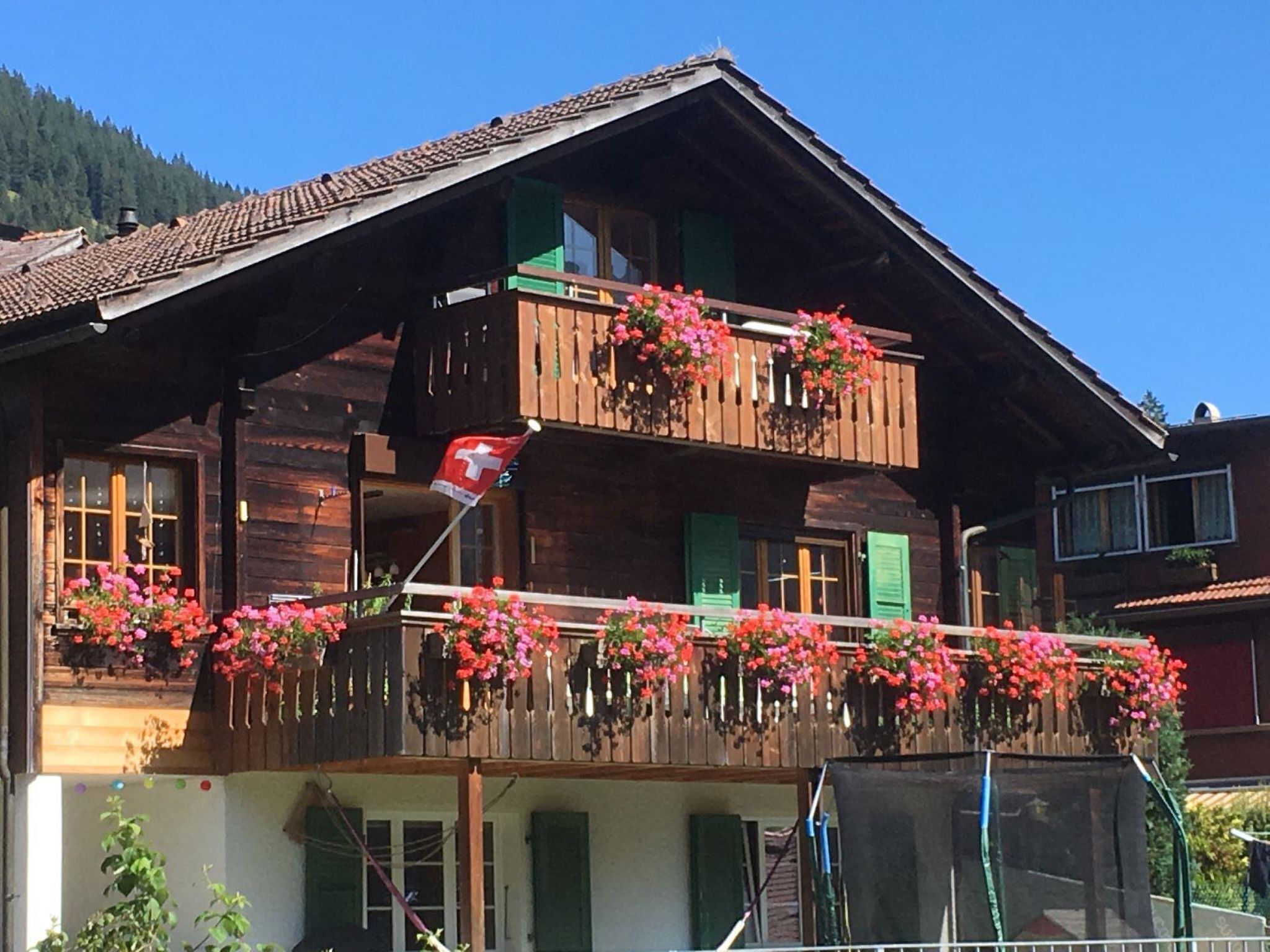 Eine Holzhütte mit Balkon, verziert mit Blumen, einer Schweizer Flagge und einem Berg im Hintergrund.