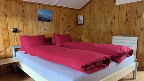 Ein Zimmer mit Holzwänden, einem Bett, einem Nachttisch und einem an der Wand befestigten Regal.