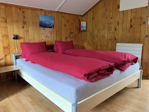 Ein Zimmer mit Holzwänden, einem Bett, einem Nachttisch und einem an der Wand befestigten Regal.