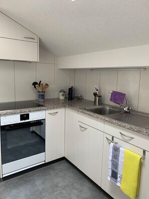 A modern kitchen with white cabinets, a built-in oven, a granite countertop, and a stainless steel sink. - Hari Appartement/Fewo, Dusche, WC, 1 Schlafraum 1.5 Zimmerwohnung by Interhome (Adelboden)