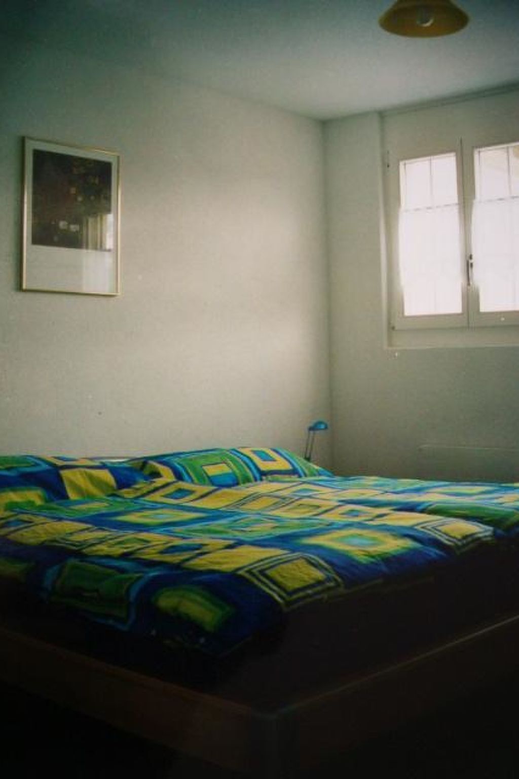A bedroom with a bed, a single wall-mounted picture, and a window with curtains.