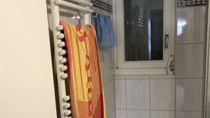 Une salle de bain avec une douche, un porte-serviettes avec plusieurs serviettes, un flacon de savon liquide et une fenêtre.