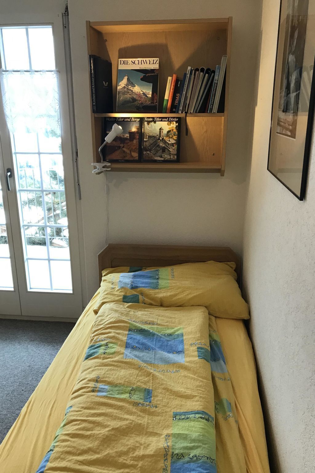 A room with a bed, a bookshelf with books, and a window.