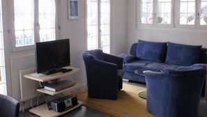 Un salon avec un téléviseur à écran plat posé sur un meuble, un canapé bleu, un fauteuil assorti et une petite table basse.