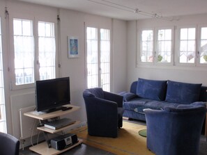 Ein Wohnzimmer mit Flachbildfernseher auf einem Schrank, einem blauen Sofa, einem passenden Sessel und einem kleinen Couchtisch.