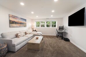 A living room with a sofa, a coffee table, a desk with a computer, and a TV. - Whitefish Mountain Retreat with Hot Tub, Fire Pit & Heated Garage (Whitefish)