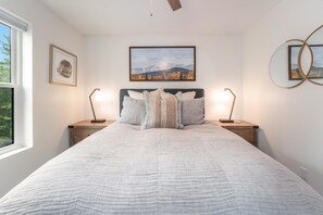 A bedroom with a large bed, two bedside tables, a wall-mounted lamp, and framed pictures. - Whitefish Mountain Retreat with Hot Tub, Fire Pit & Heated Garage (Whitefish)