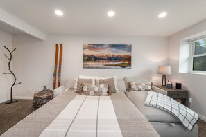 Une chambre à coucher avec un grand lit, un tableau représentant un paysage de montagne, une lampe et une fenêtre donnant sur un beau panorama.