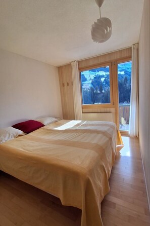 A bedroom with a large bed, a window with a view of a snowy landscape, and a ceiling light fixture. - Chalet Sirius Appartement/Fewo, Bad, WC, 3 Schlafräume 4-Zimmer-Wohnung by Interhome (Adelboden)