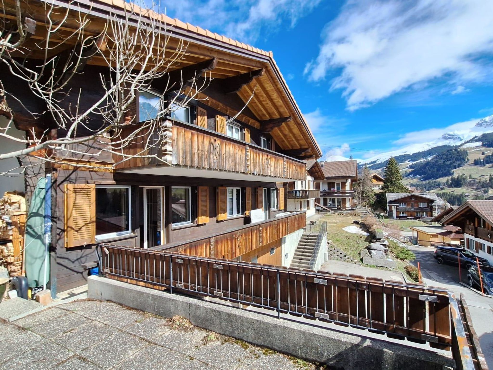 Eine zweistöckige Holzchalet mit Balkon, Steinstufen und Blick auf die umliegende Berglandschaft.