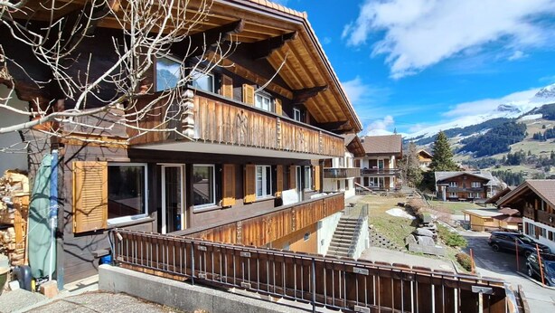 A two-story wooden chalet with a balcony, a stone staircase, and a view of the surrounding mountainous landscape. - Chalet Sirius Appartement/Fewo, Bad, WC, 3 Schlafräume 4-Zimmer-Wohnung by Interhome (Adelboden)