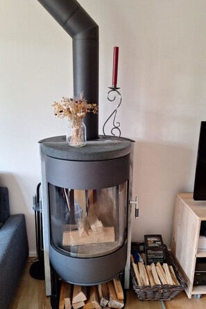 A modern wood-burning stove with a glass door, a red candle holder, and a vase with dried flowers on top. - Chalet Sirius Appartement/Fewo, Bad, WC, 3 Schlafräume 4-Zimmer-Wohnung by Interhome (Adelboden)