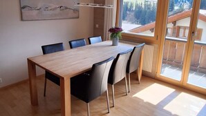 A spacious dining area with a wooden table and chairs, a large window with a view of a mountainous landscape, and a modern pendant light. - Chalet Sirius Appartement/Fewo, Bad, WC, 3 Schlafräume 4-Zimmer-Wohnung by Interhome (Adelboden)