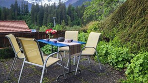 An outdoor seating area with a table and chairs, surrounded by greenery and a mountainous backdrop. - Chalet Sirius Appartement/Fewo, Bad, WC, 3 Schlafräume 4-Zimmer-Wohnung by Interhome (Adelboden)