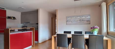 Una cucina moderna con mobili rossi, un'area pranzo con tavolo in legno e sedie nere, e un'ampia finestra con vista.