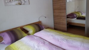 A bedroom with a bed, pillows, a wooden wardrobe, a mirror, and a wall art piece. - Grüneggli Appartement/Fewo, Bad, WC, 2 Schlafräume 3.Zimmerwohnung by Interhome (Adelboden)