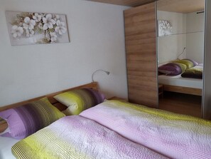 A bedroom with a bed, pillows, a wooden wardrobe, a mirror, and a wall art piece. - Grüneggli Appartement/Fewo, Bad, WC, 2 Schlafräume 3.Zimmerwohnung by Interhome (Adelboden)