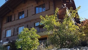 A multi-story wooden building with balconies, surrounded by rocks and shrubs. - Grüneggli Appartement/Fewo, Bad, WC, 2 Schlafräume 3.Zimmerwohnung by Interhome (Adelboden)
