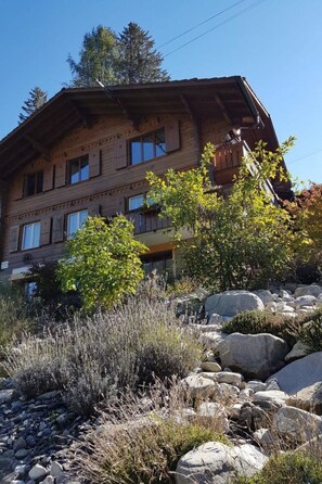 A multi-story wooden building with balconies, surrounded by rocks and shrubs. - Grüneggli Appartement/Fewo, Bad, WC, 2 Schlafräume 3.Zimmerwohnung by Interhome (Adelboden)
