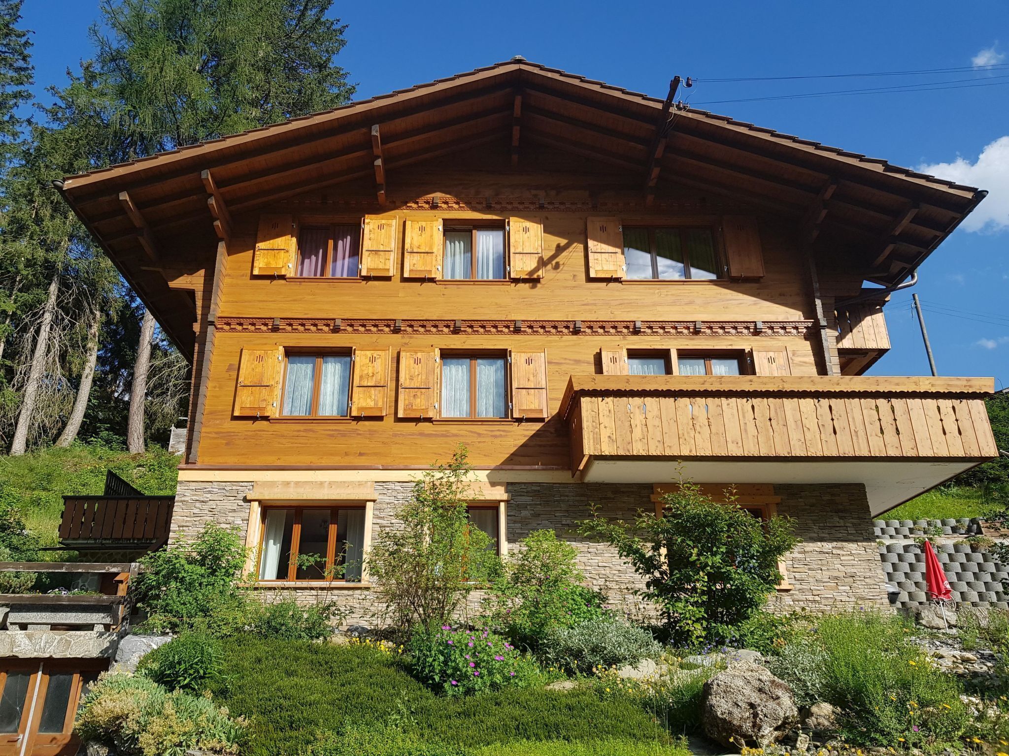 En flervånings chalet byggd av trä, med ett sluttande tak, en grund av sten och en balkong.