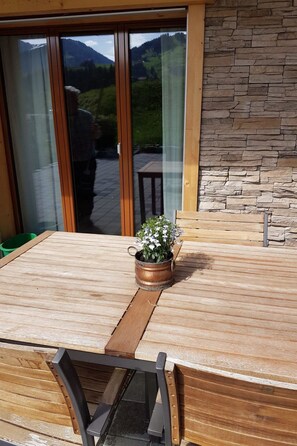 A wooden table with a potted plant, a chair, and a view of a mountainous landscape through a glass door. - Grüneggli Appartement/Fewo, Bad, WC, 2 Schlafräume 3.Zimmerwohnung by Interhome (Adelboden)