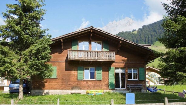 Eine Holzhütte mit Balkon, grünen Fensterläden und einem eingezäunten Hof.