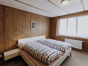 Ein Schlafzimmer mit Holzwänden, einem Bett mit floralem Bettbezug, einem Nachttisch und einem Fenster mit Vorhängen.