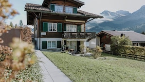 Ein zweistöckiges Holzhaus mit Balkon, einer gepflasterten Auffahrt und Bergblick.
