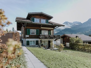 Ein zweistöckiges Holzhaus mit Balkon, einer gepflasterten Auffahrt und Bergblick.