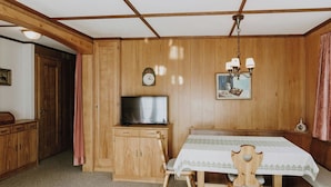Ein Zimmer mit Holzvertäfelung, einem Fernseher, einer Uhr und einem Tisch mit Stühlen.