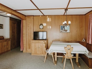 Ein Zimmer mit Holzvertäfelung, einem Fernseher, einer Uhr und einem Tisch mit Stühlen.