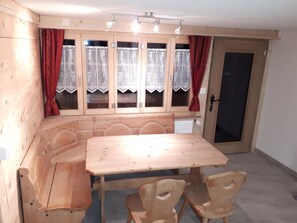 A wooden dining area with a table and chairs, a window with curtains, and a door. - Wanni Appartement/Fewo, Bad, WC, 3 Schlafräume 4-Zimmerwohnung by Interhome (Frutigen)