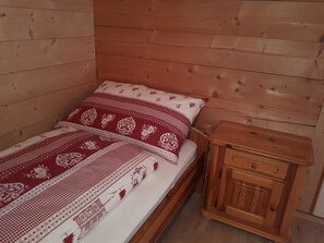 A single bed with a patterned bedspread and pillows, a wooden nightstand with a drawer, and wooden walls. - Wanni Appartement/Fewo, Bad, WC, 3 Schlafräume 4-Zimmerwohnung by Interhome (Frutigen)
