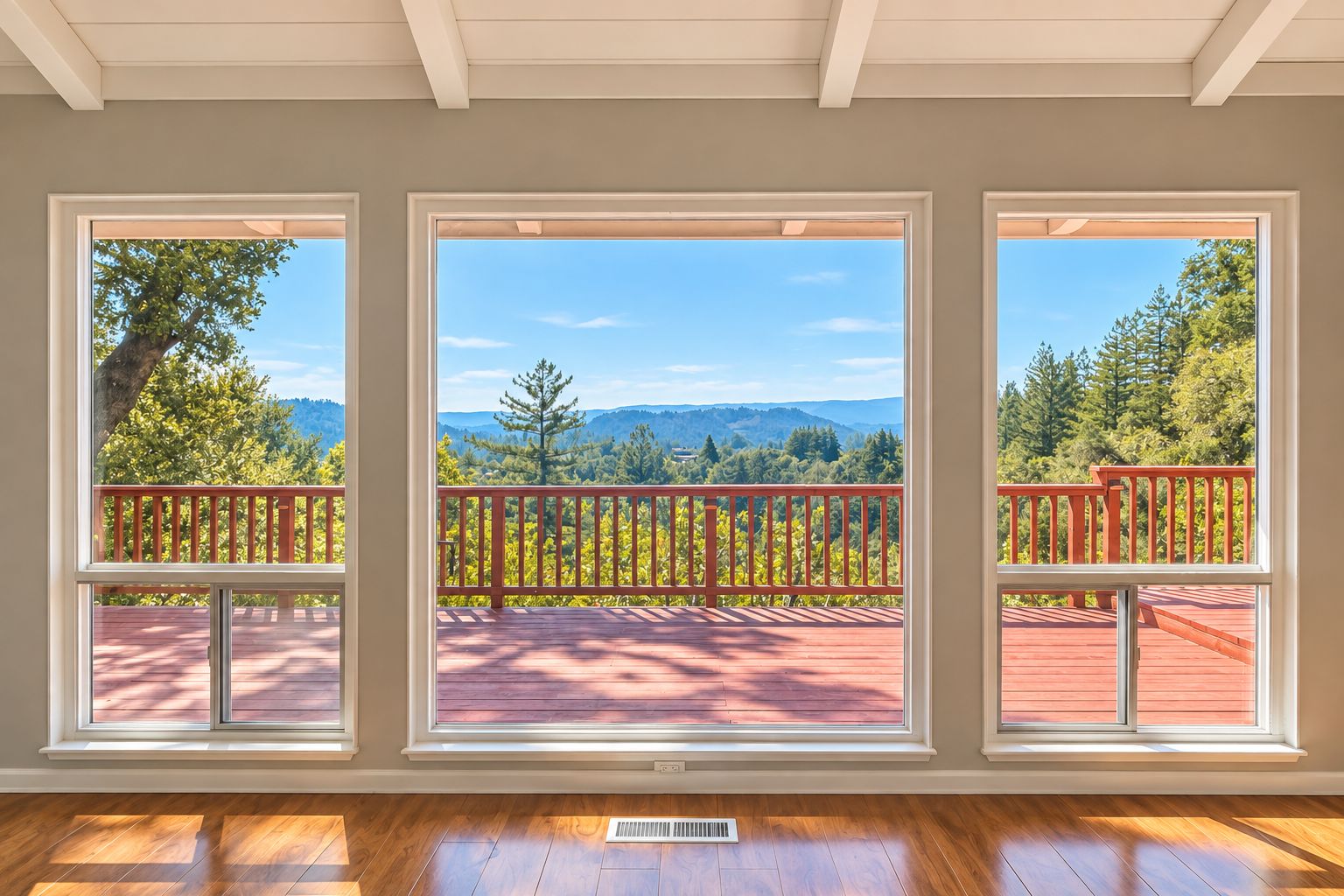 A room with three large windows offering a view of a deck and surrounding greenery.