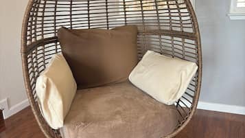 Une chaise ronde, faite d’un matériau tressé, dotée d’un siège et d’un dossier rembourrés, et dont les pieds sont blancs.