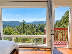 A bedroom with a large window offering a view of a forested landscape. - Hidden Vista House, Mountain Views & 2 Primary Suites (Los Gatos)
