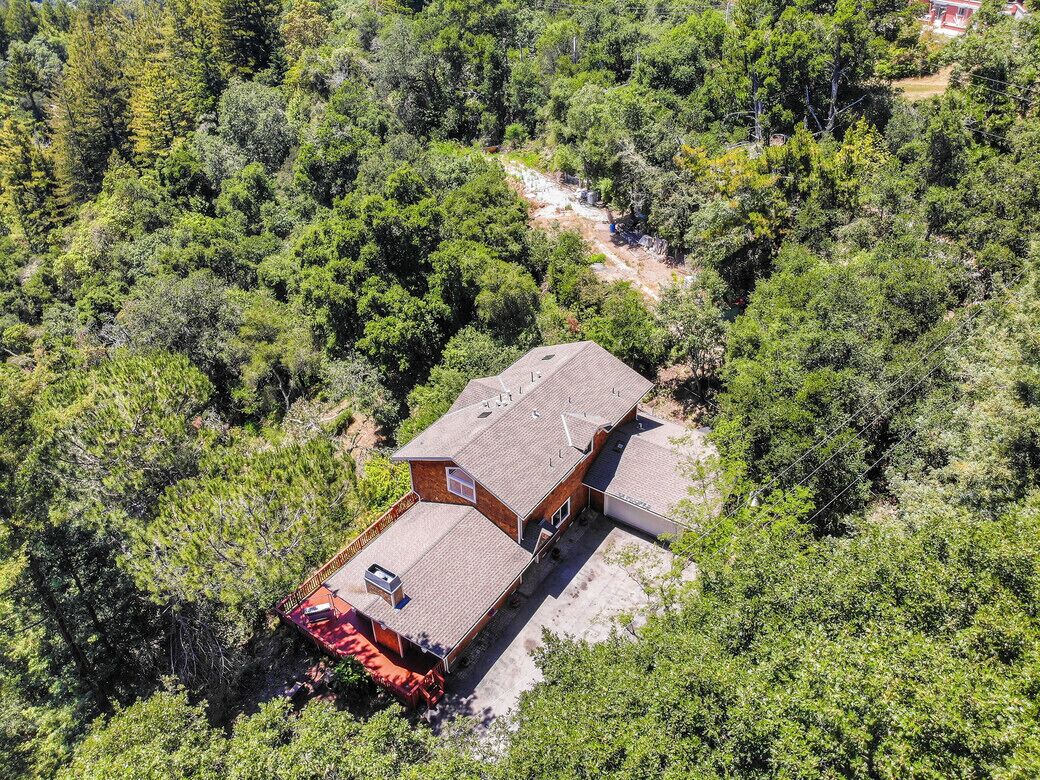 A two-story house with a flat roof, surrounded by dense forest.
