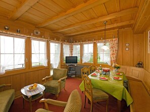 A wooden-paneled room with a dining table set for four, chairs, a television, and large windows. - Mi Casa Appartement/Fewo, Bad, WC, 3 Schlafräume 3-Zimmerwohnung 1.Stock by Interhome (Adelboden)