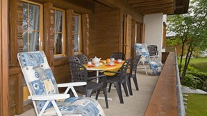 Een buitenterras met houten vloerdelen, een tafel met stoelen en uitzicht op het groen.