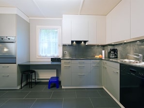 Eine moderne Küche mit grauen Schränken, einem eingebauten Backofen, einer Kaffeemaschine und einem Fenster mit leichten Vorhängen.