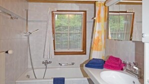 Een badkamer met een bad, douche, wastafel en raam.