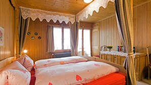 Een kamer met houten lambrisering, een bed, gordijnen, een radiator en een tafel met een vaas.